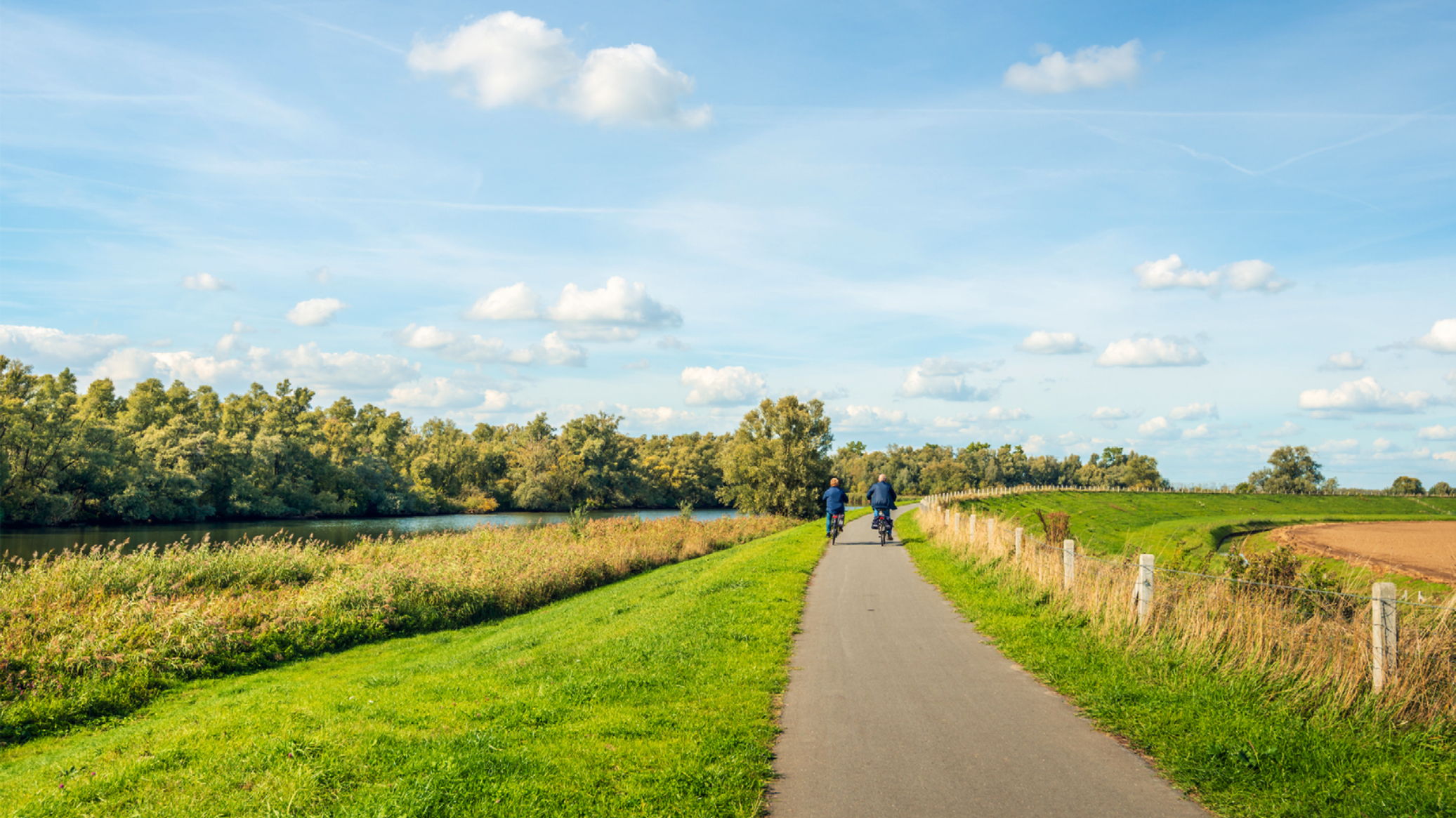 Twee fietsers fietsen naast elkaar op een dijk naast het water.